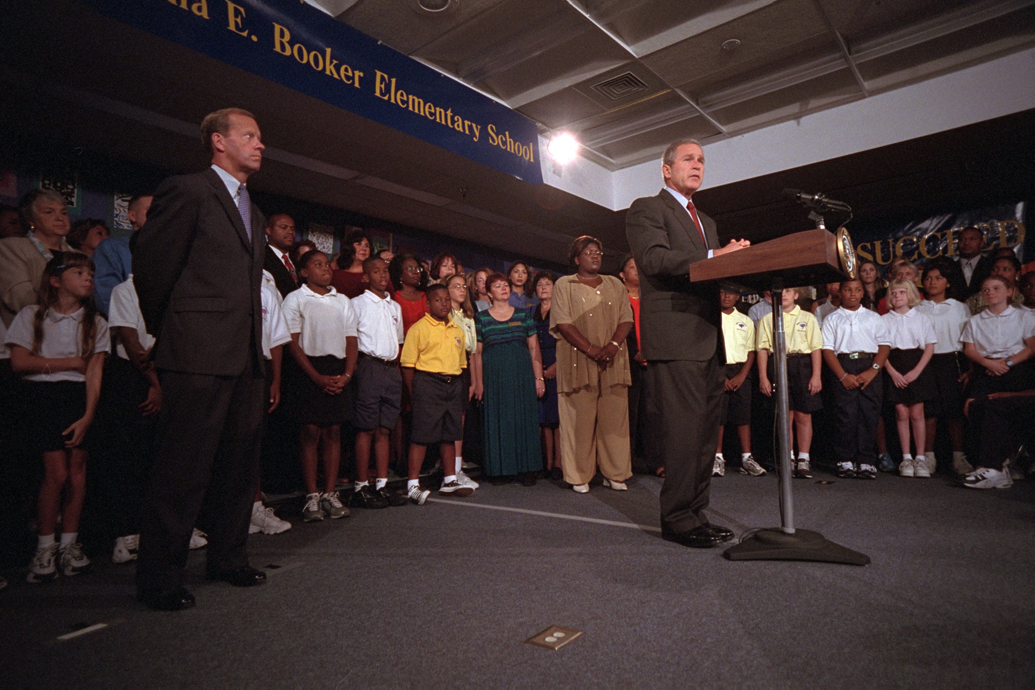President George W. Bush stands at a podium with children standing around him