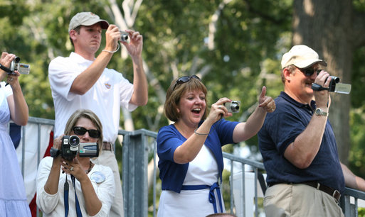 Spectators hold cameras and cheer on the tee ball players