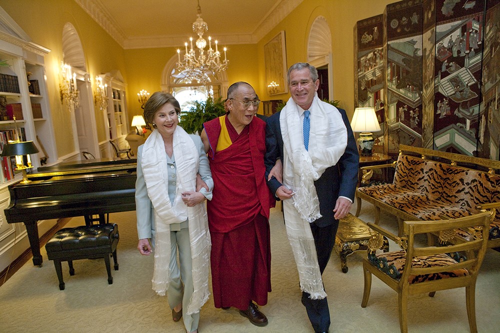 Wearing the traditional white Tibetan scarves presented to them upon his greeting, President George W. Bush and Mrs. Laura Bush walk with the Dalai Lama through the Center Hall of the Private Residence at the White House.