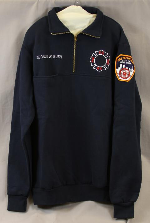 Zippered pullover, navy fleece embroidered with "George W. Bush" and "FDNY" in white and red, "Fire Department, City of New York" patch on sleeve. POTUS wore the pullover to throw out the first pitch at the 2001 World Series baseball game in Yankee Stadium. (DO.183824)
