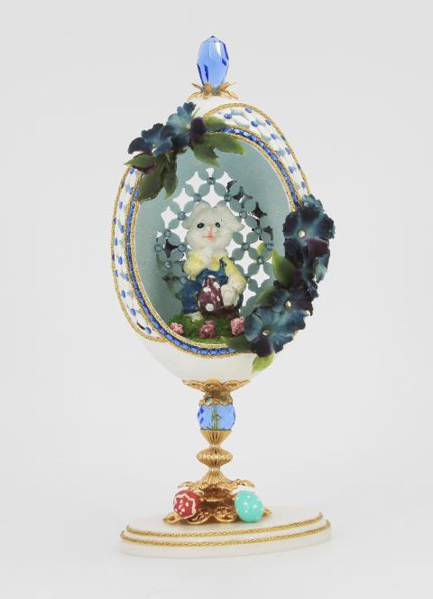 Green, white, and blue hand carved egg with an Easter bunny inside and affixed with rhinestones, miniature eggs, and flowers.