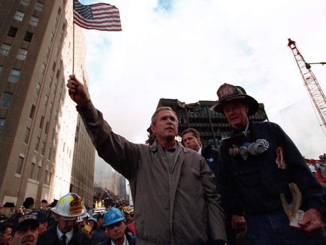 Standing upon the ashes of the terrorist attacks upon the World Trade Center with retired firefighter Bob Beckwith from Ladder 117, President George W. Bush waves an American flag, September 14, 2001, after addressing recovery workers in New York City. (P7376-22)