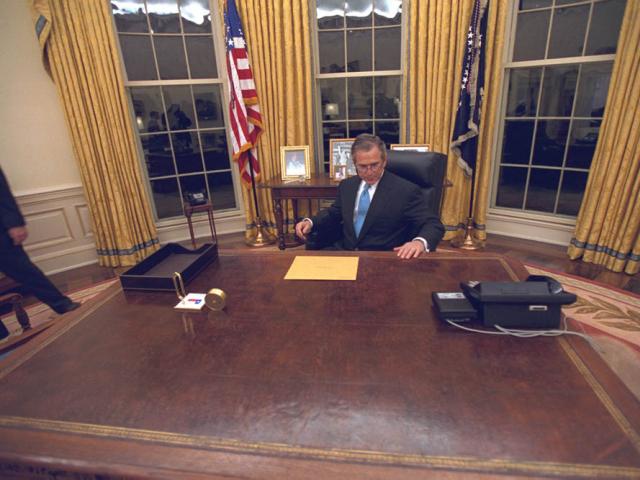 President George W. Bush sits at the Resolute Desk in the Oval Office to read the transition letter from President William J. Clinton, January 20, 2001.