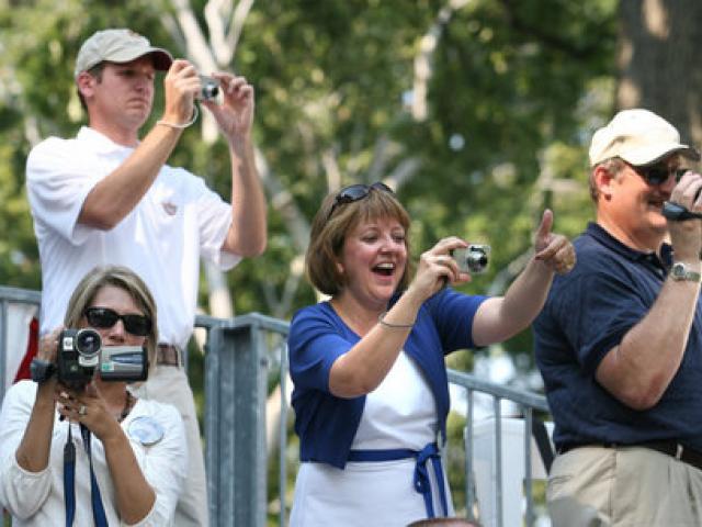 Spectators hold cameras and cheer on the tee ball players
