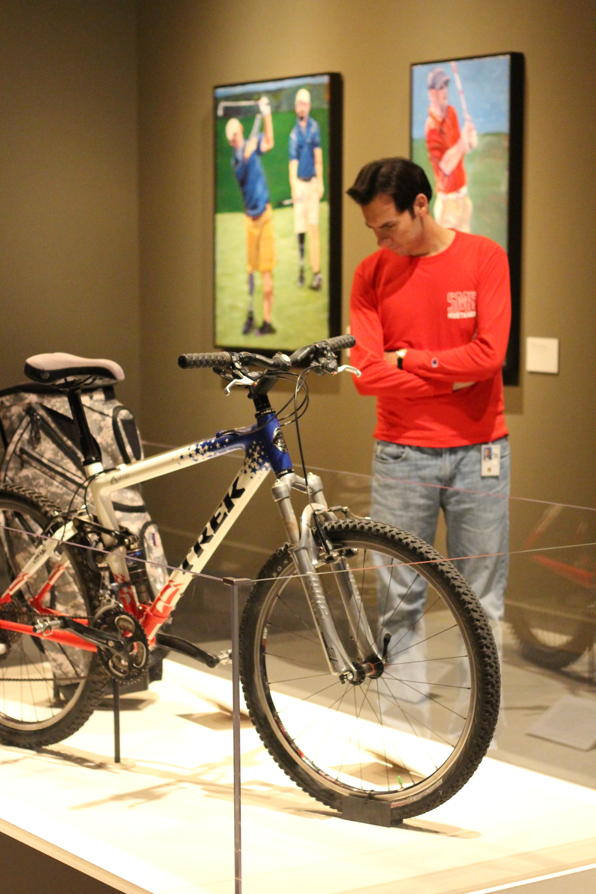 Photo of a visitor looking at the trek bicycle and golf back from the Portraits of Courage exhibit at the George W Bush Library and Museum