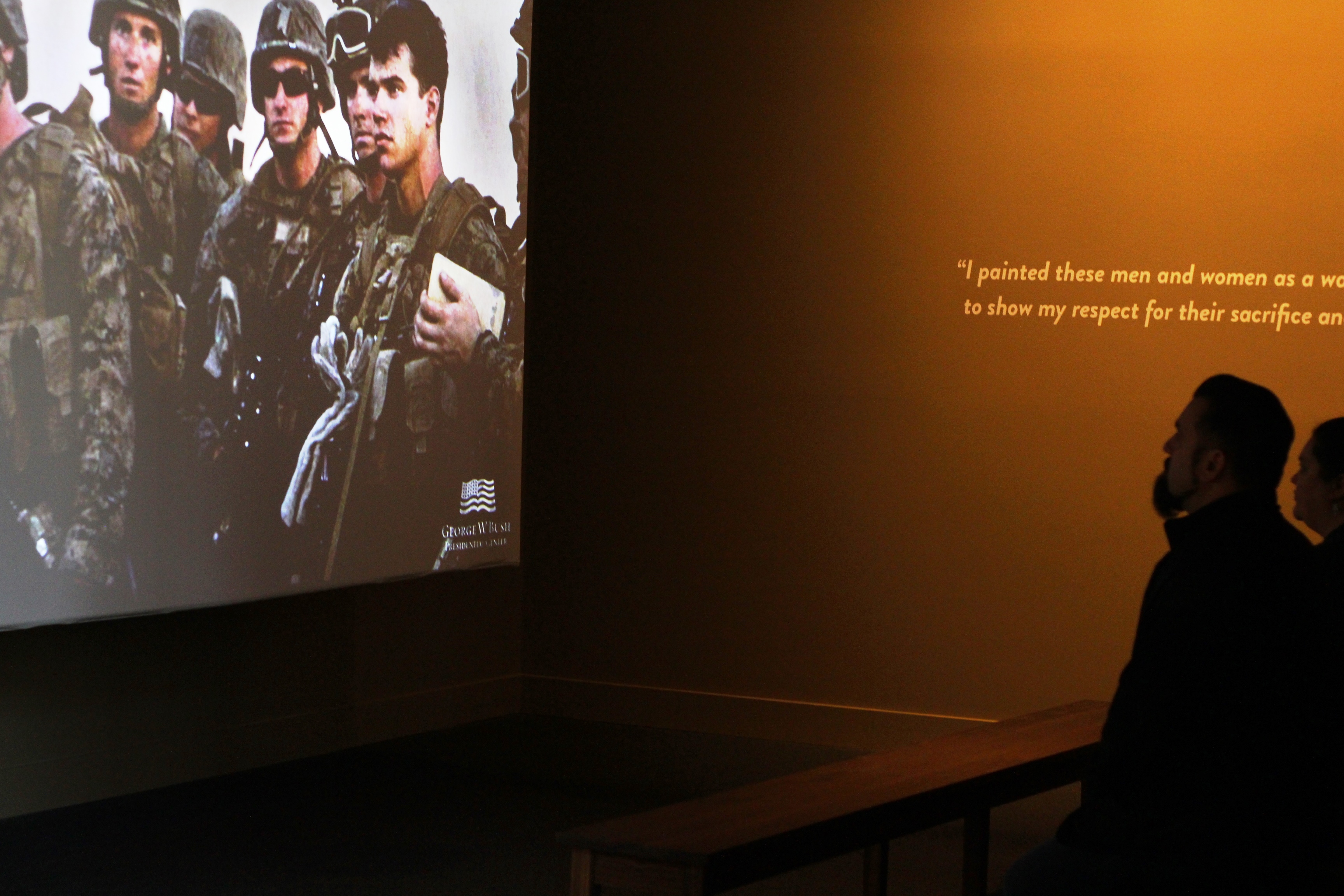 A photo of a visitors watching a short movie as part of the 2017 Portraits of Courage exhibit at the George W Bush Library and Museum.