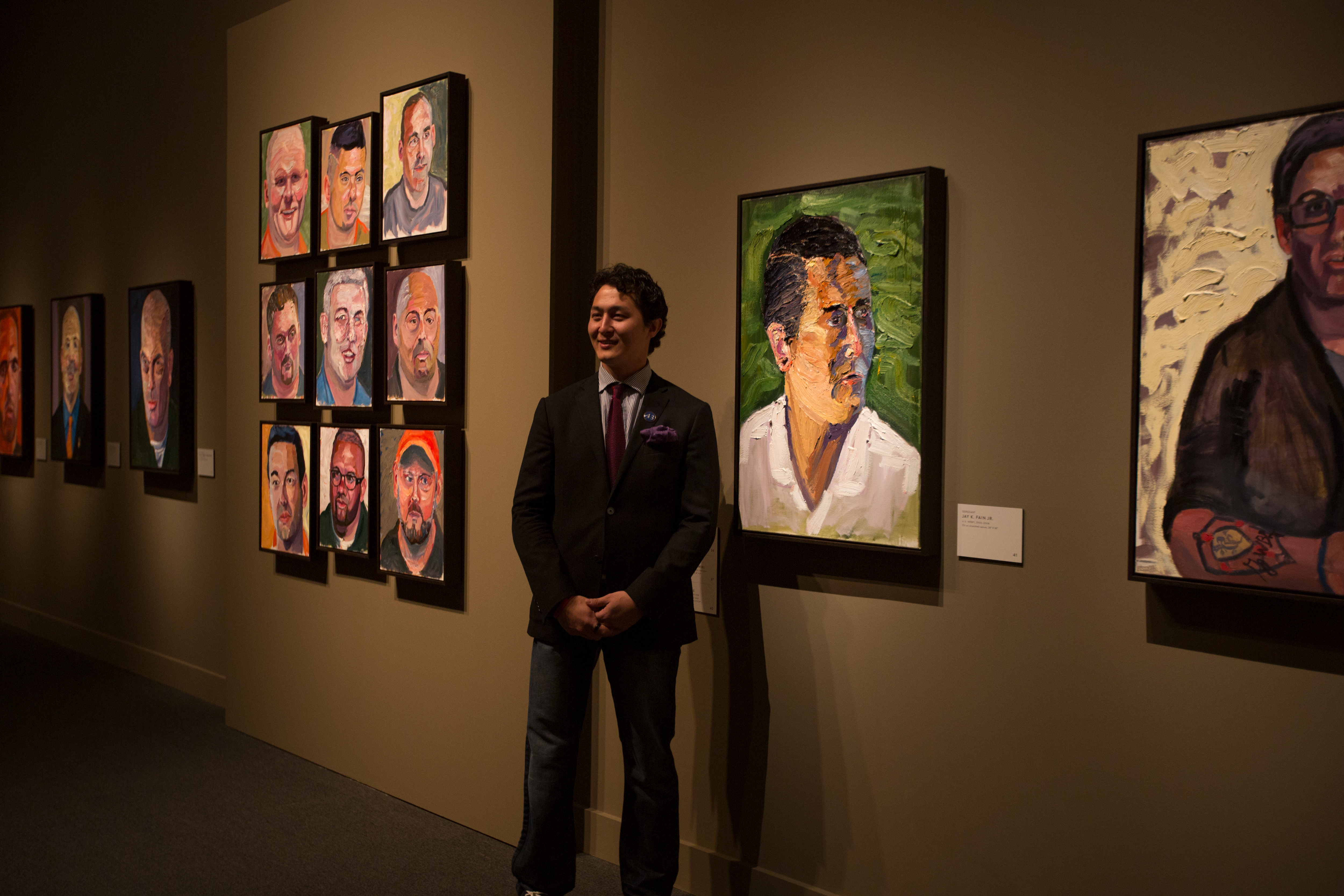 A photo of one of George W Bush's portrait subjects standing by his painting at the 2017 Portraits of Courage exhibit at the George W Bush Library and Museum.