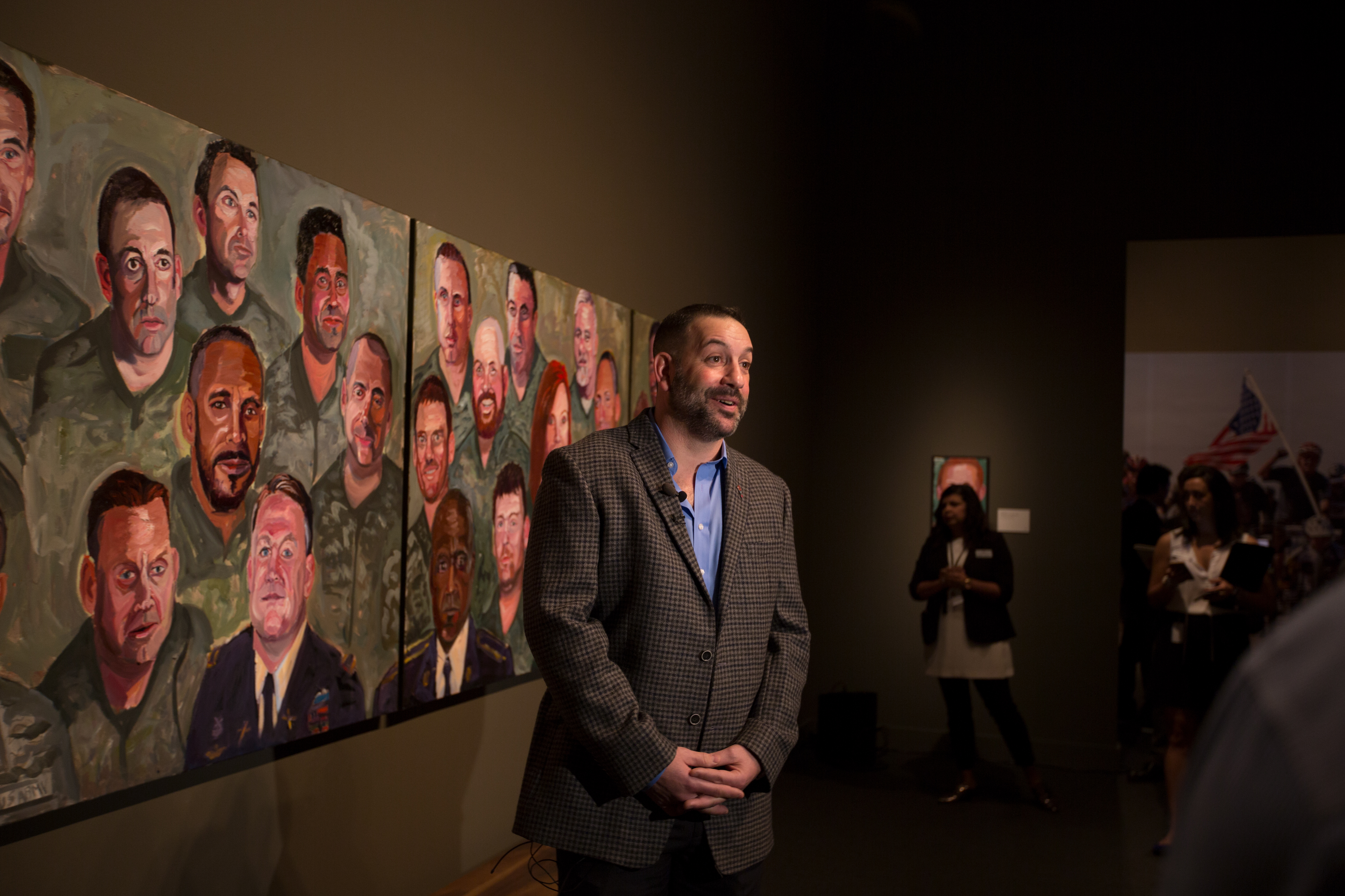 A photo of a man being filmed near his portrait and others painted by President George W Bush, part of the 2017 exhibit Portraits of Courage, at the George W Bush Library and Museum