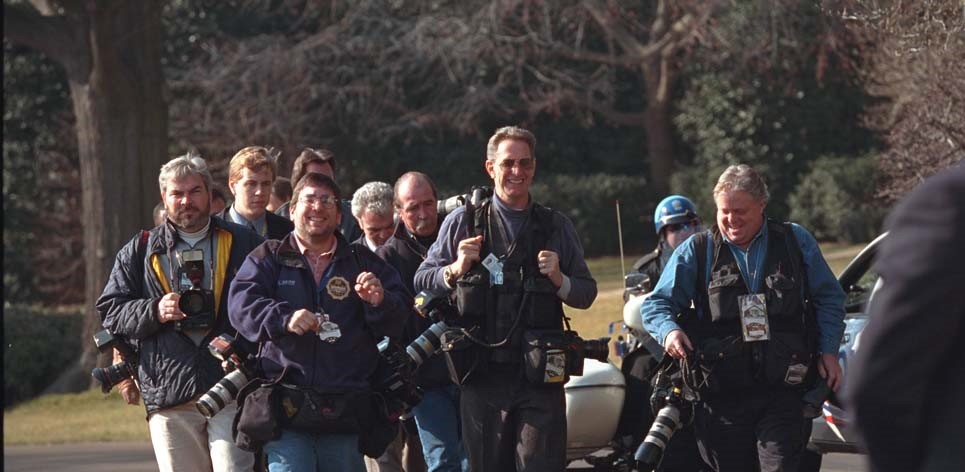 Members of the press walk next to each other on White House grounds