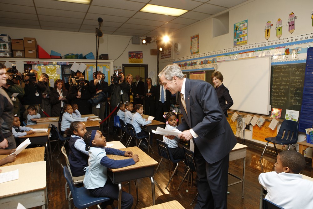 President George W. Bush stands in a classroom with students and press