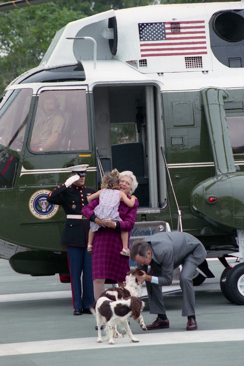 President and Mrs. Bush disembark from Marine One and are greeted by their granddaughter, Ellie LeBlond, and their dogs, Millie and Ranger, August 10, 1990. George Bush Presidential Library and Museum. P15074-22.