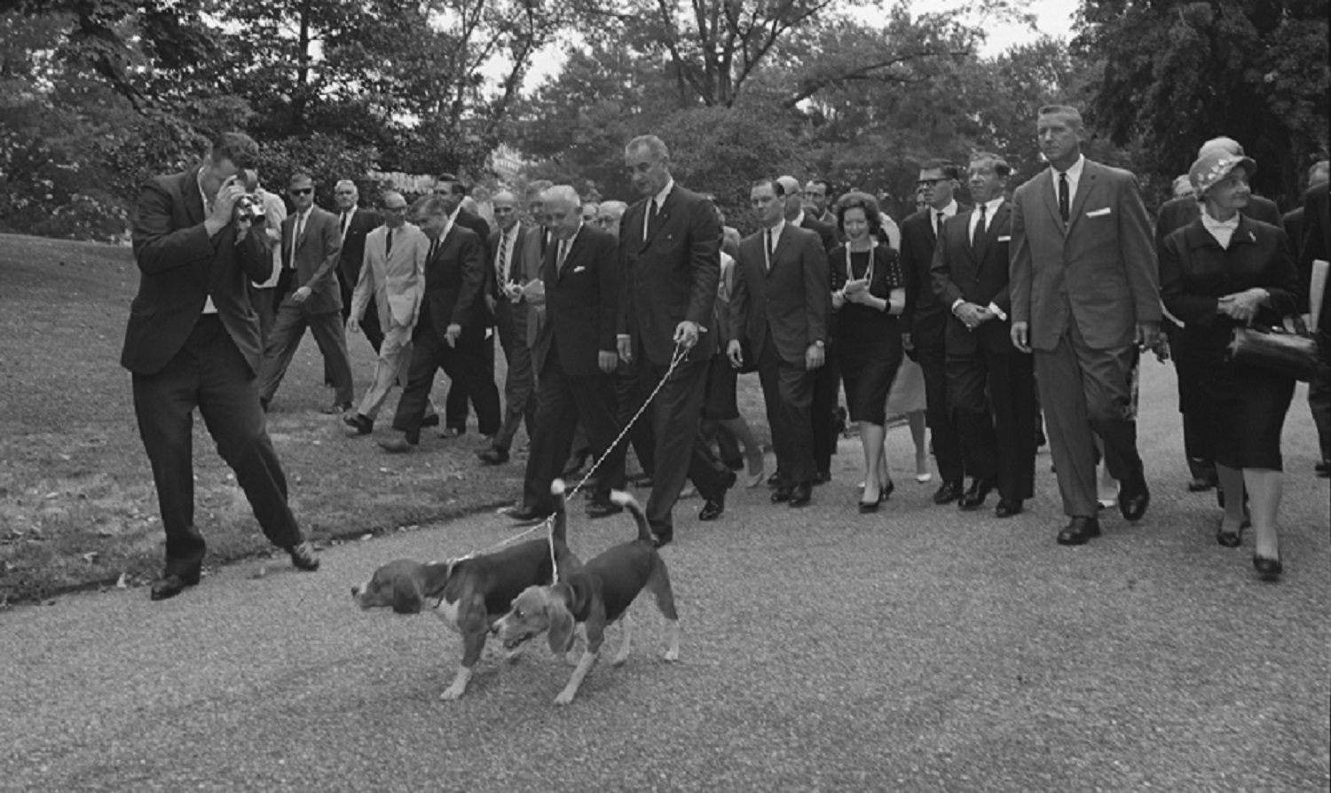 President Lyndon B. Johnson walks his two beagles as a large group of press members follow, Washington DC, August 18, 1964. LBJ Library photo by Cecil Stoughton. 336-2-WH64.
