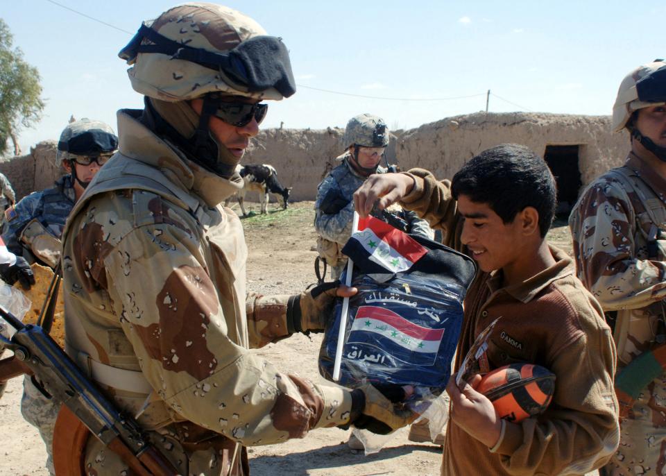 An Iraqi Army (IA) Soldier gives a local Iraqi boy a new Iraqi national flag and a new school backpack in 2006.