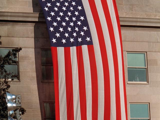 As inspiration for fellow rescue workers searching through debris, firefighters unfurl a large American flag over the scarred stone of the Pentagon, September 12, 2001. (P7244-27)