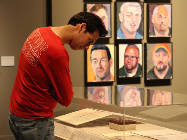 A photo of a visitor looking at items in a display case with portraits hanging on the wall in the background, part of the 2017 exhibit Portraits of Courage, at the George W Bush Library and Museum 