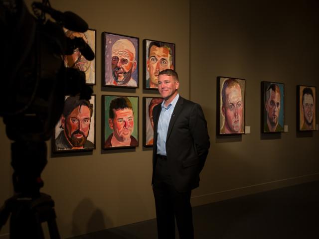 A photo of one of George W Bush's portrait subjects being interviewed near his painting at the 2017 Portraits of Courage exhibit at the George W Bush Library and Museum.