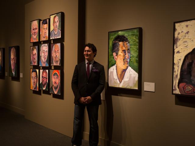 A photo of one of George W Bush's portrait subjects standing by his painting at the 2017 Portraits of Courage exhibit at the George W Bush Library and Museum.