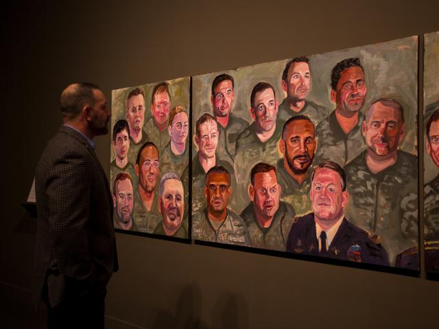 A photo of a man looking at his portrait in a mural painted by President Bush, part of the 2017 Portraits of Courage exhibit at the George W Bush Library and Museum.