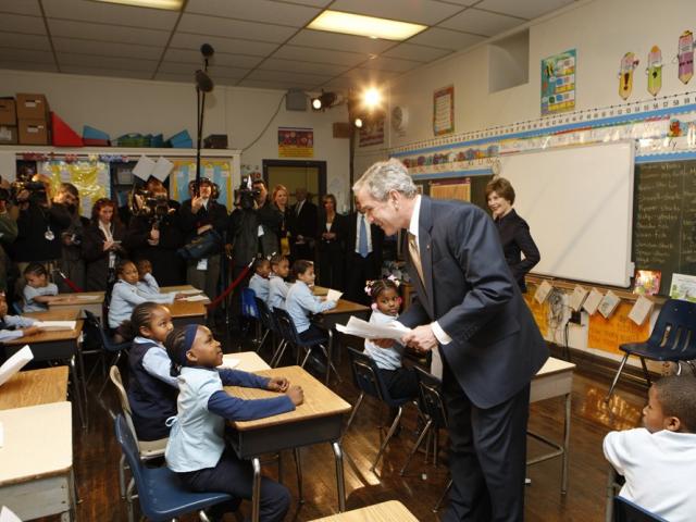 President George W. Bush stands in a classroom with students and press