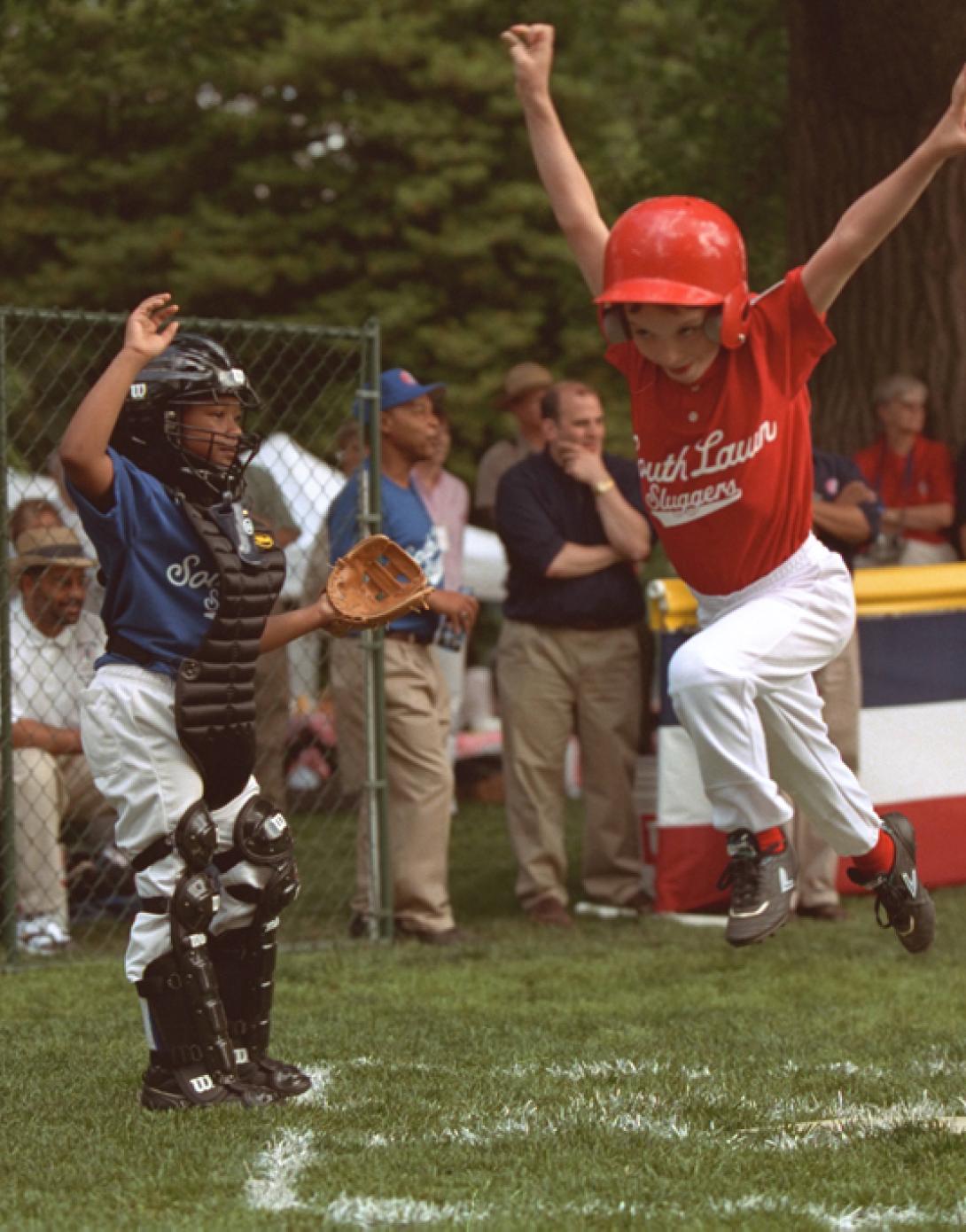 A tee ball player leaps in the air as he crosses home.