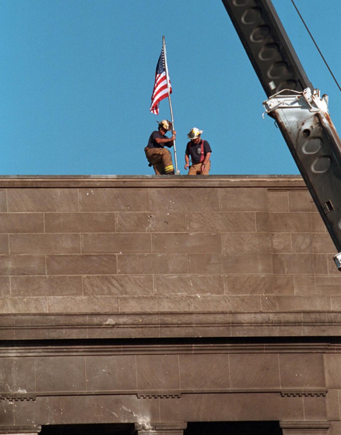 Echoing the actions of the soldiers who raised the flag in victory at Iwo Jima during World War II, firefighters post the American flag directly into the scarred stone of the Pentagon, September 12, 2001, in Arlington, Virginia. (P7244-22)