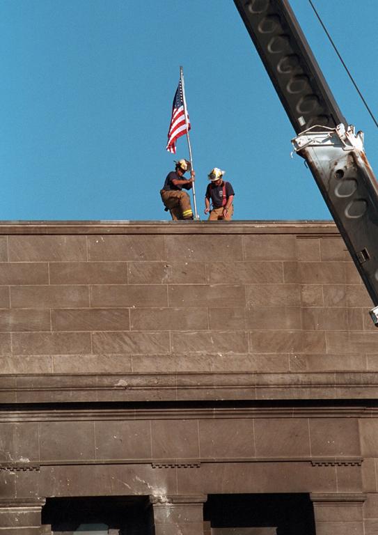 Echoing the actions of the soldiers who raised the flag in victory at Iwo Jima during World War II, firefighters post the American flag directly into the scarred stone of the Pentagon, September 12, 2001, in Arlington, Virginia. (P7244-22)