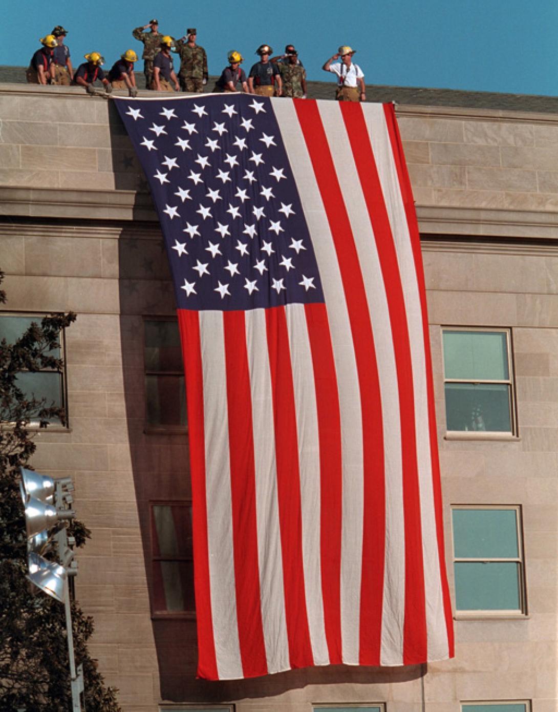 As inspiration for fellow rescue workers searching through debris, firefighters unfurl a large American flag over the scarred stone of the Pentagon, September 12, 2001. (P7244-27)