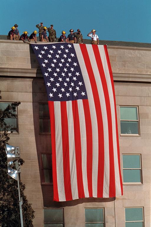 As inspiration for fellow rescue workers searching through debris, firefighters unfurl a large American flag over the scarred stone of the Pentagon, September 12, 2001. (P7244-27)