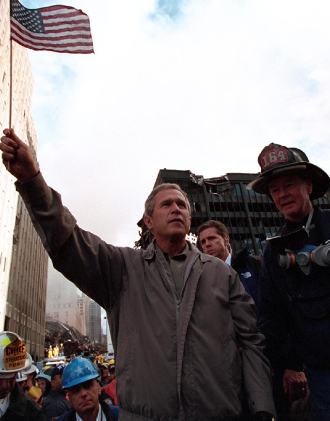 Standing upon the ashes of the terrorist attacks upon the World Trade Center with retired firefighter Bob Beckwith from Ladder 117, President George W. Bush waves an American flag, September 14, 2001, after addressing recovery workers in New York City. (P7376-22)
