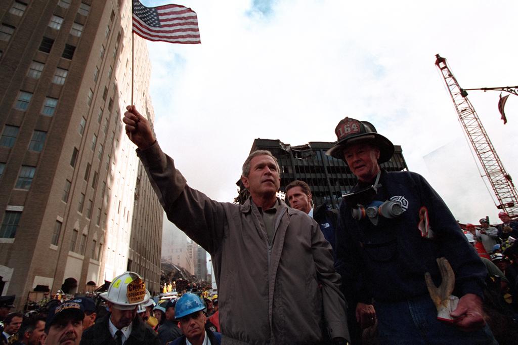 Standing upon the ashes of the terrorist attacks upon the World Trade Center with retired firefighter Bob Beckwith from Ladder 117, President George W. Bush waves an American flag, September 14, 2001, after addressing recovery workers in New York City. (P7376-22)