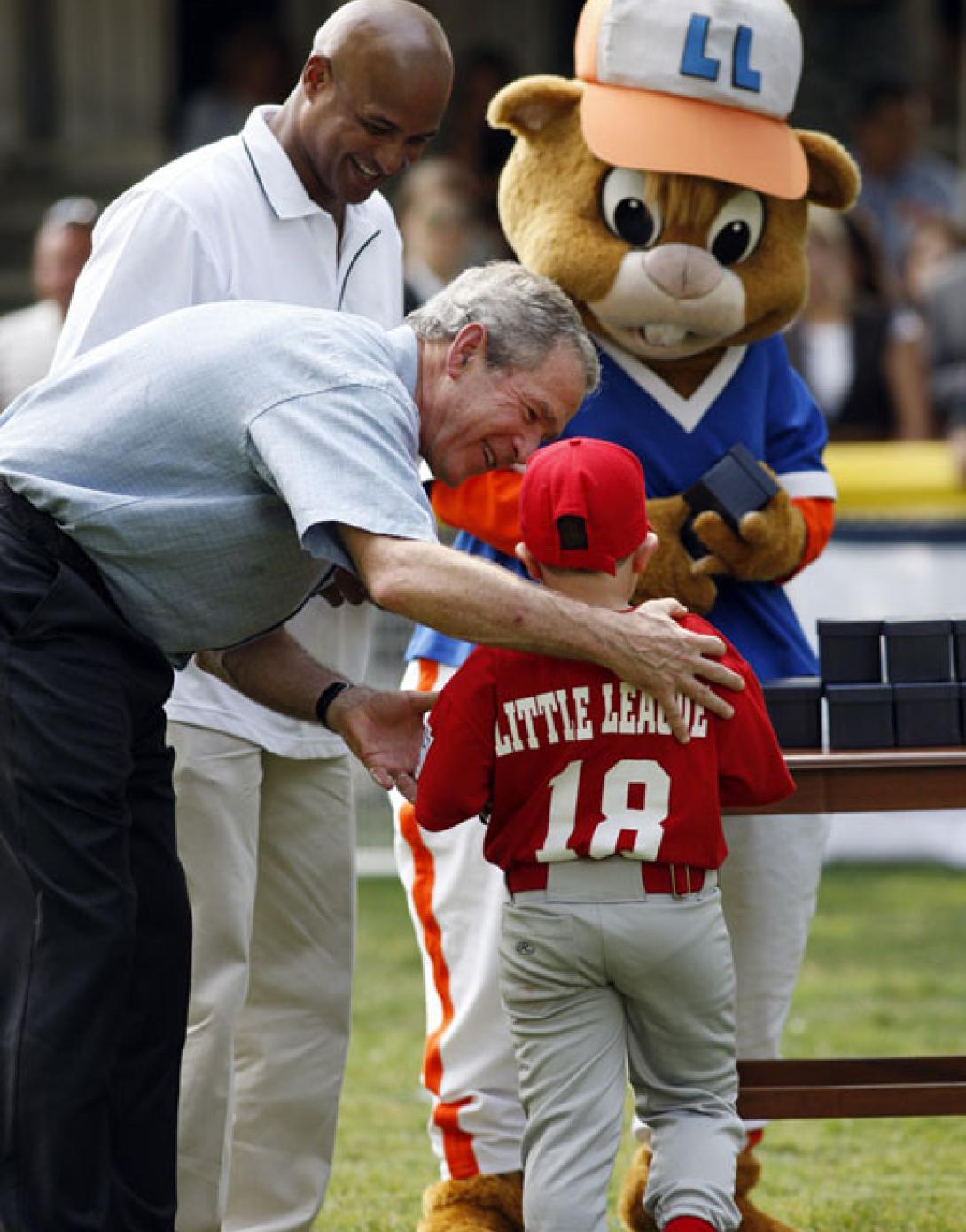 President George W. Bush presents Angel Tavarez with a baseball. President Bush is joined on the field by Roberto Clemente, Jr. and Dugout, the Little League mascot.