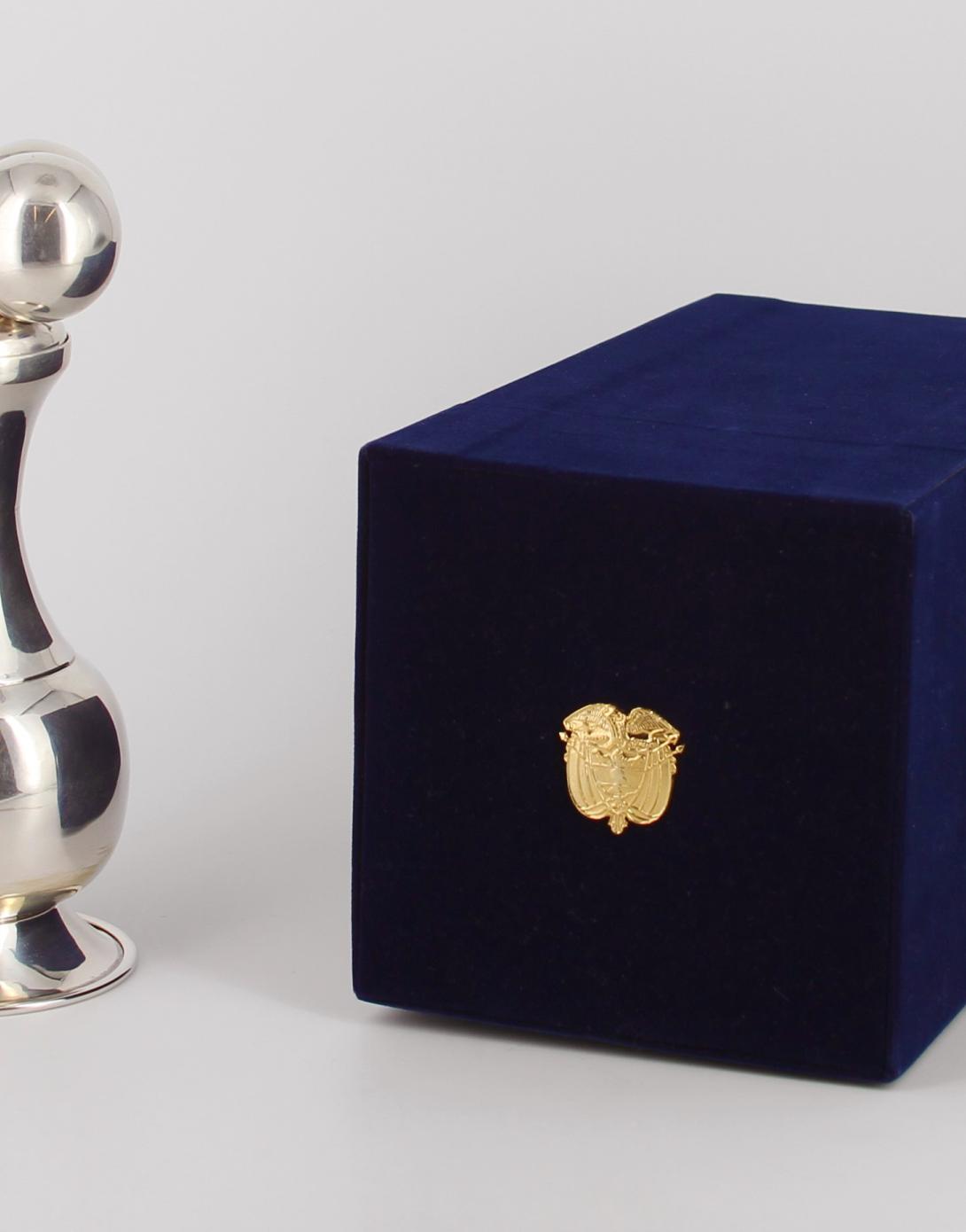 Silver container with removable lid that represents an indigenous artifact; held in a blue velvet hinged box with the coat of arms of Colombia on the lid. Presented to President Bush during a working visit to Washington, D. C. in 2007. Gifted by Alvaro Uribe, President of the Republic of Colombia.
