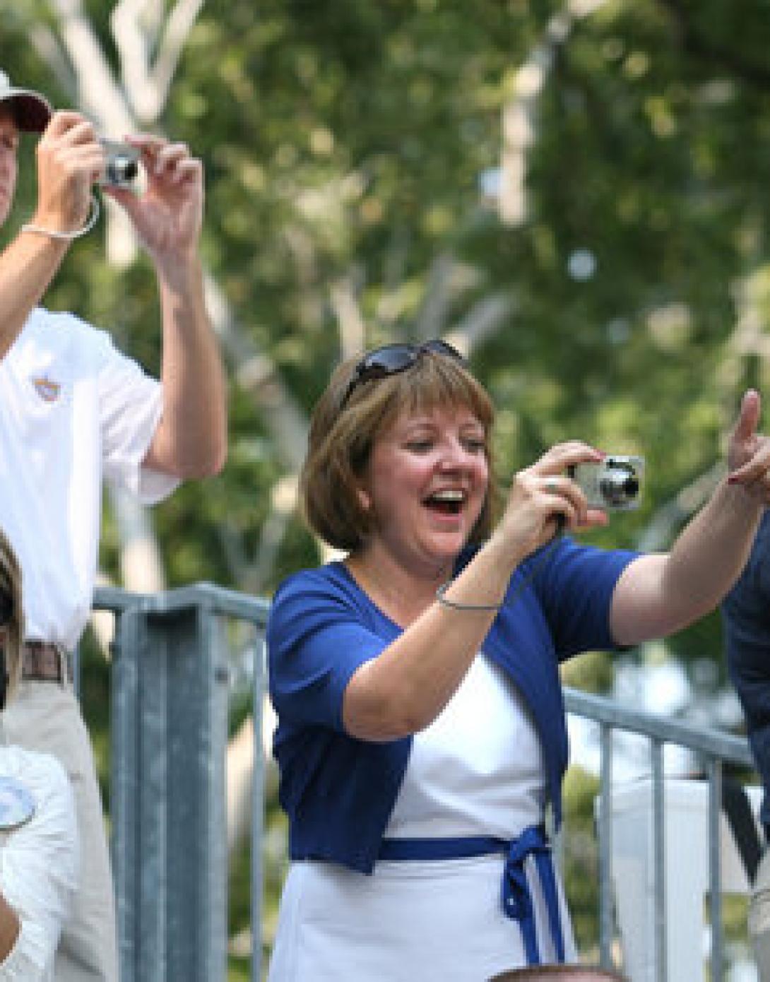 Spectators hold cameras and cheer on the tee ball players