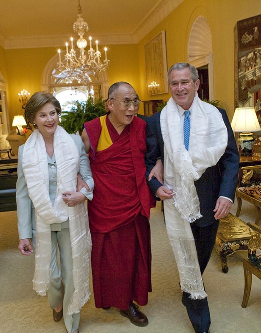 Wearing the traditional white Tibetan scarves presented to them upon his greeting, President George W. Bush and Mrs. Laura Bush walk with the Dalai Lama through the Center Hall of the Private Residence at the White House.